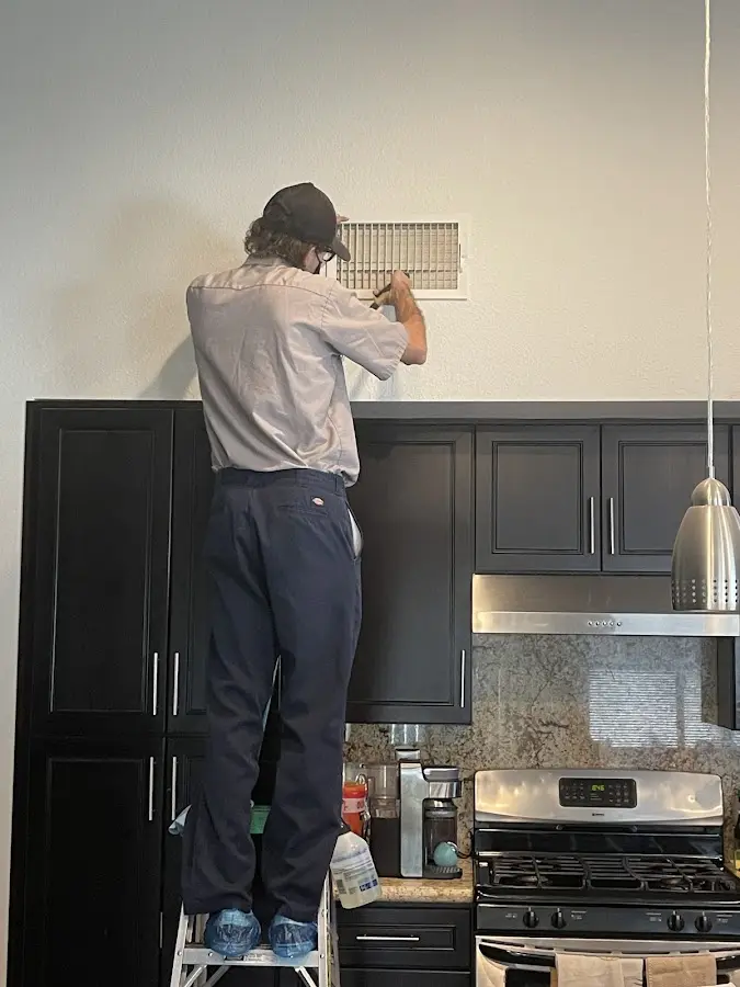 Technician inspecting an air vent during HVAC service in Helotes